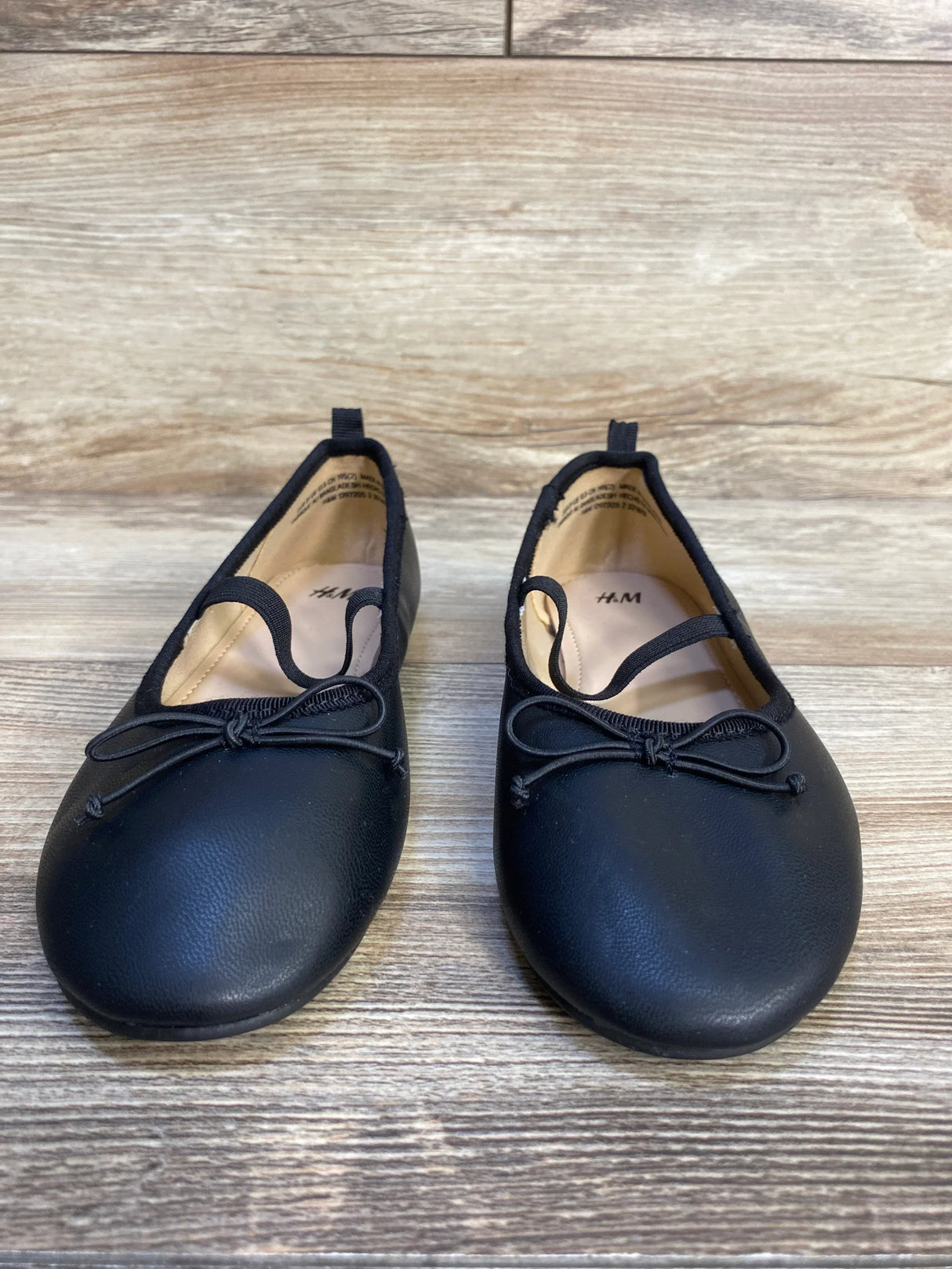 Black girls' ballet flats with bow detail on wooden floor, kids casual dress shoes