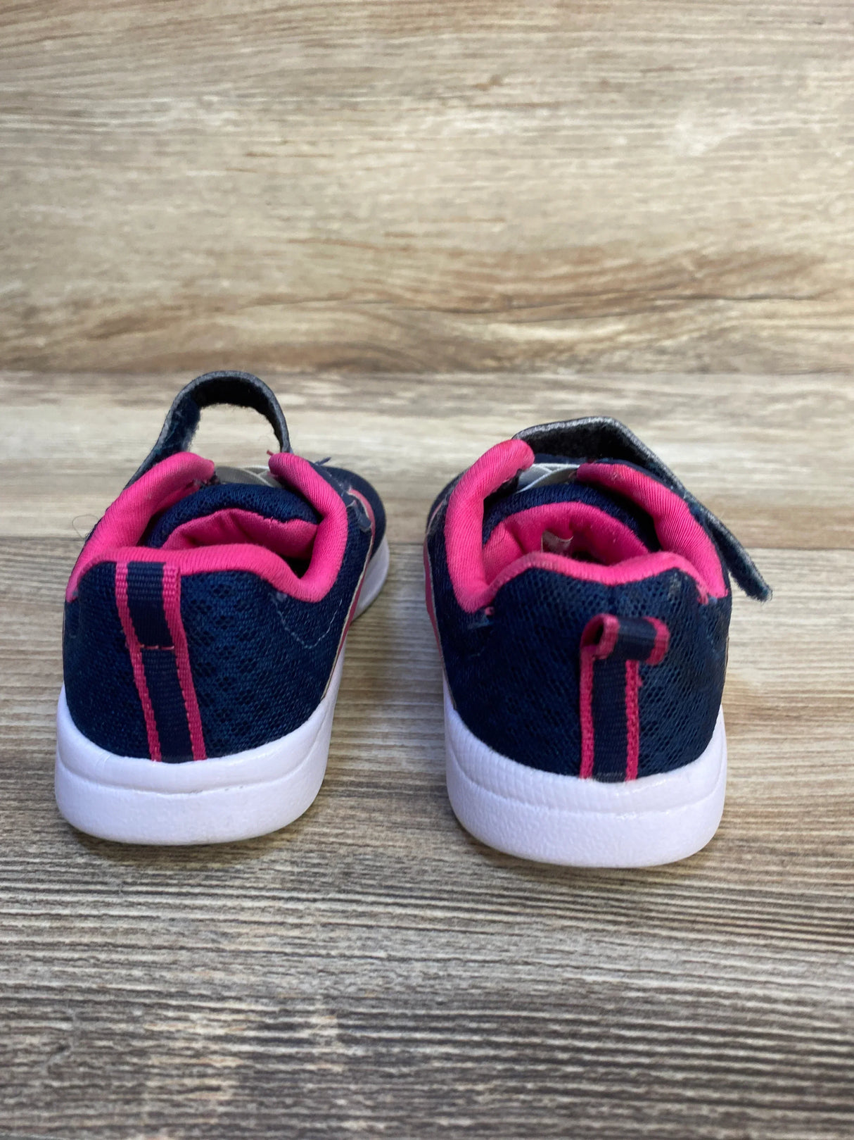Rear view of navy blue and pink toddler sneakers with white soles on wooden floor