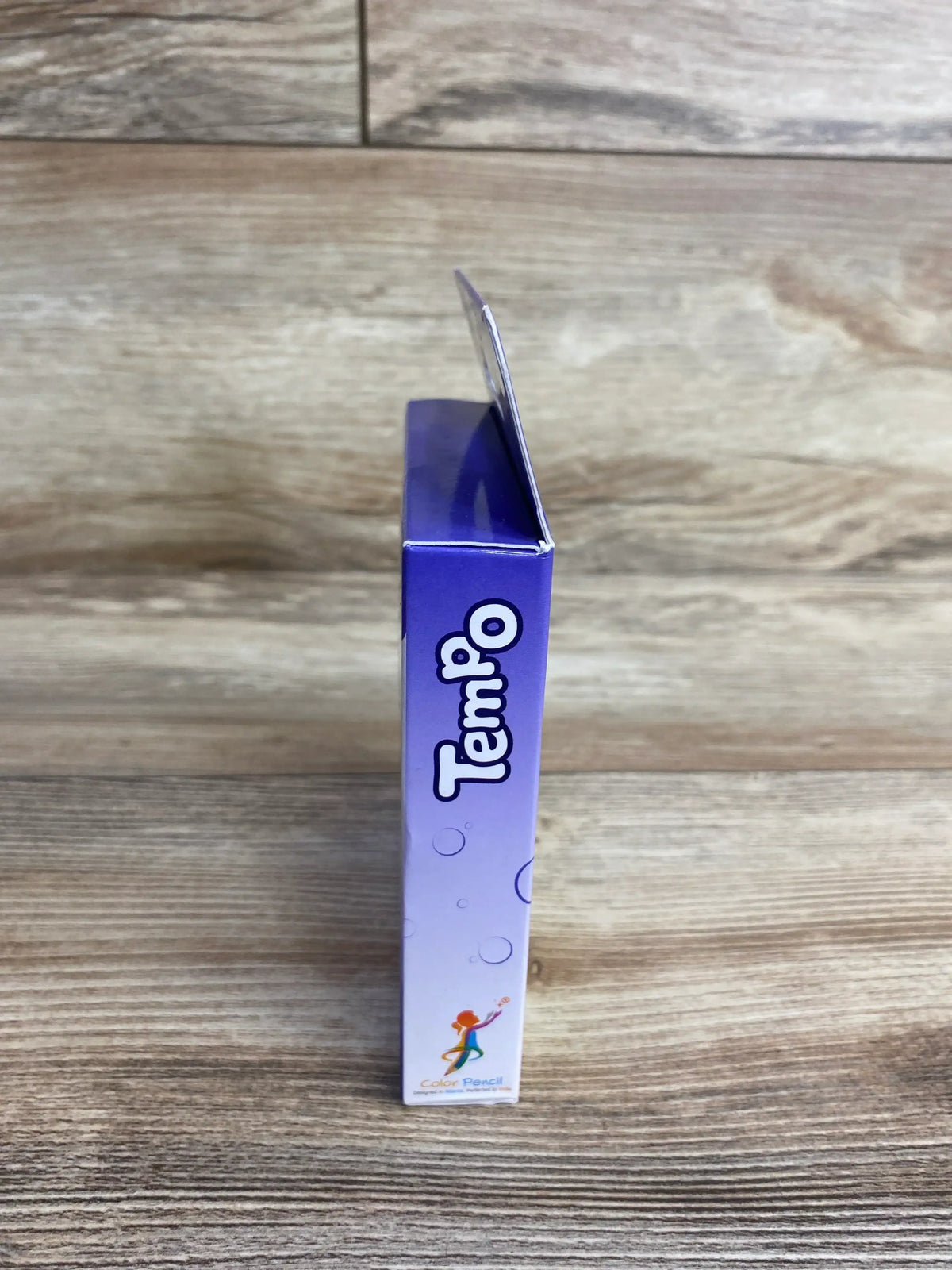 Purple Tempo color pencil box standing on wood surface, side view with playful design