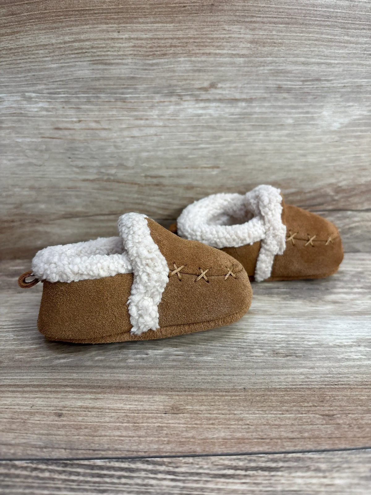 Brown suede baby shoes with white fleece lining on wooden background