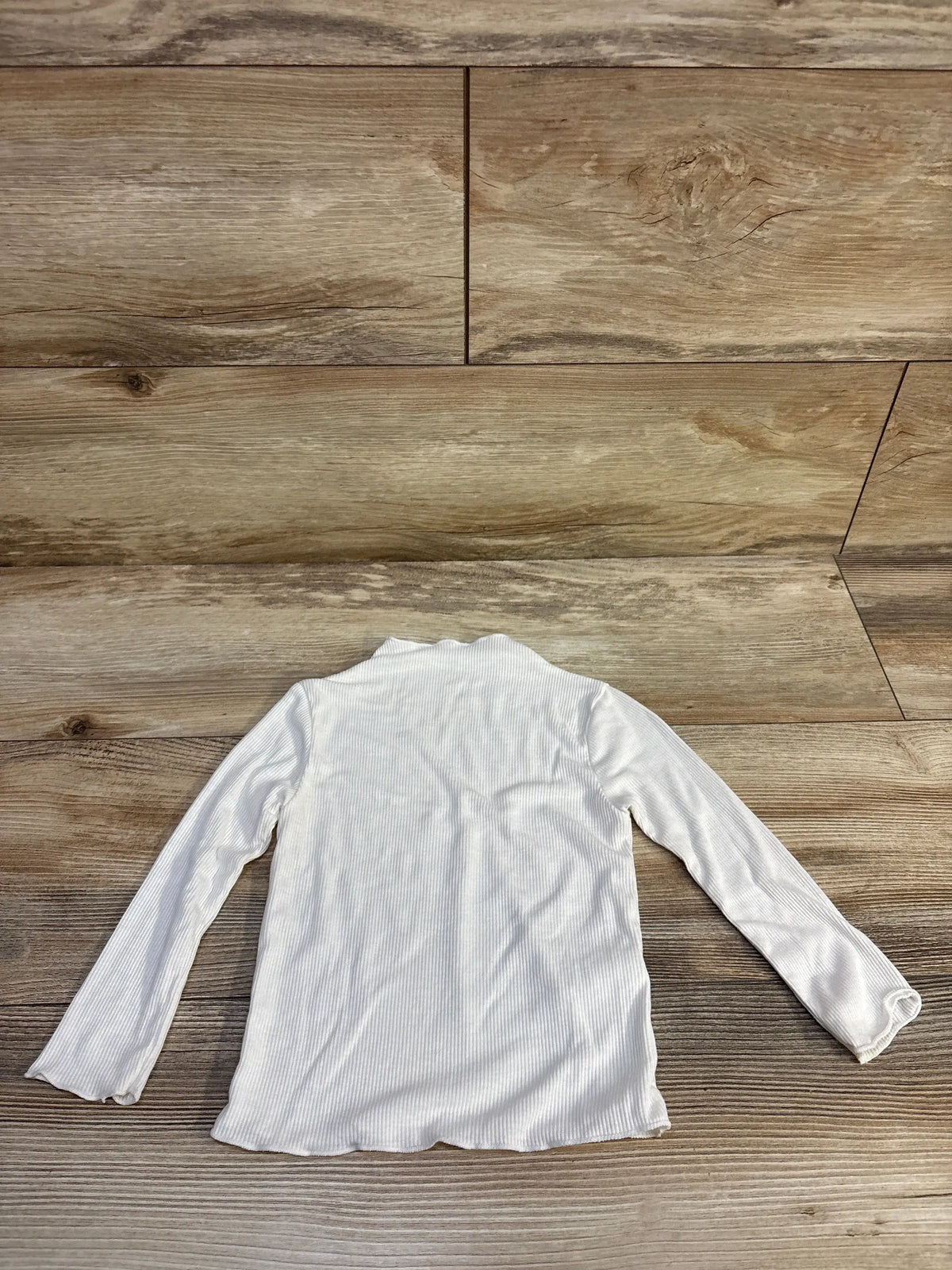 Back view of white ribbed turtleneck shirt size 2T showing long sleeves and ribbed texture on wood background