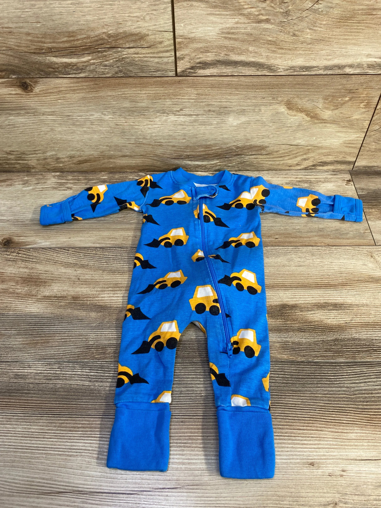 Flat-lay of blue convertible sleeper with yellow construction truck print, front zipper and fold-over foot cuffs on wood floor background