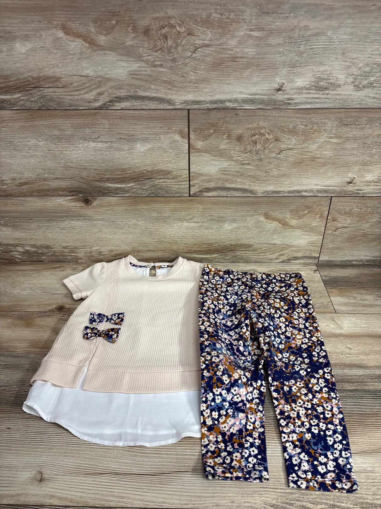 Flat lay of Bonnie Jean top and leggings set in natural, size 4T, with layered white hem, bow details, and navy floral leggings
