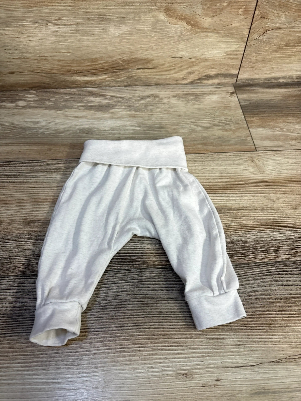 Front view of H&M white baby pants, size 3 months, showcasing foldover waistband and ribbed cuffs on wood floor
