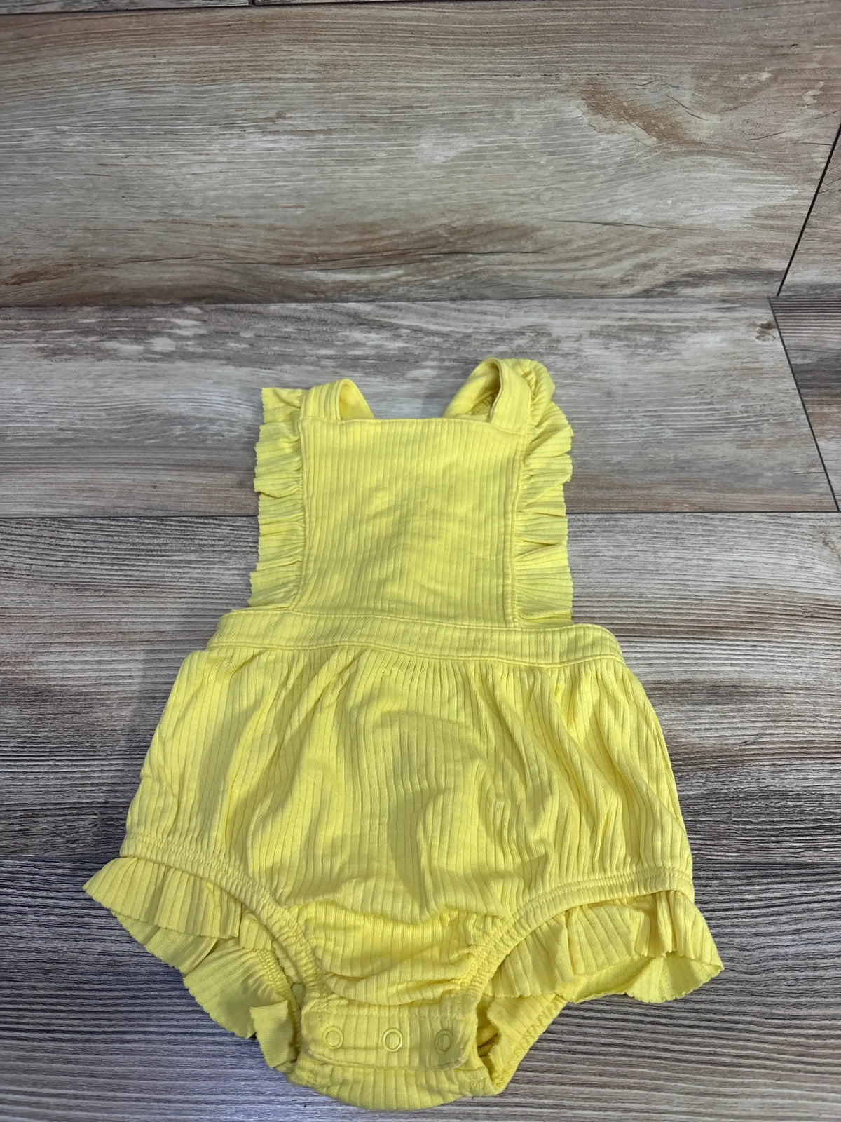 Front flat lay of yellow ribbed bubble romper size 12M with ruffled straps, snap crotch, and skirt on wood floor