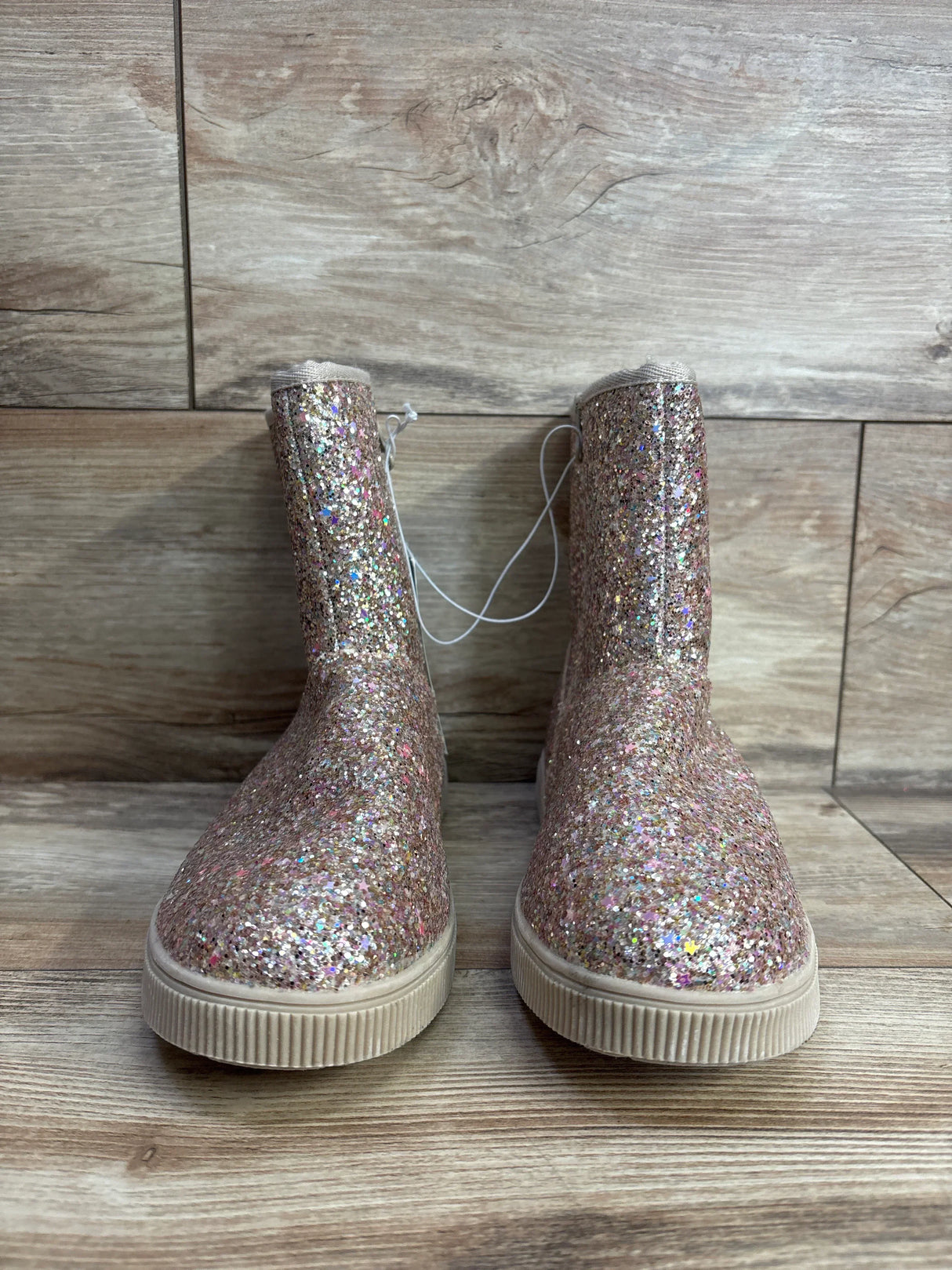Pair of children's pink glitter boots with rubber soles on wood floor