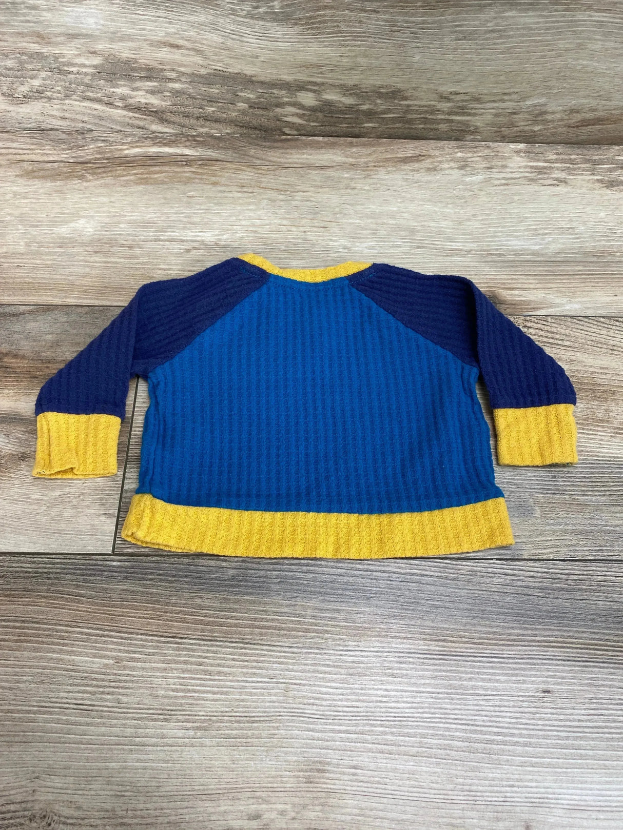 Flat lay of Cat and Jack waffle-knit shirt with blue body, navy raglan sleeves and yellow cuffs and hem on wood background