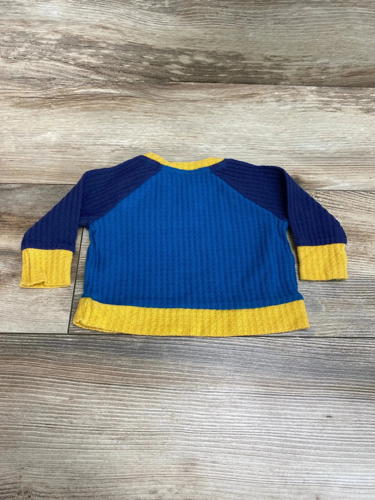 Flat lay of Cat and Jack waffle-knit shirt with blue body, navy raglan sleeves and yellow cuffs and hem on wood background