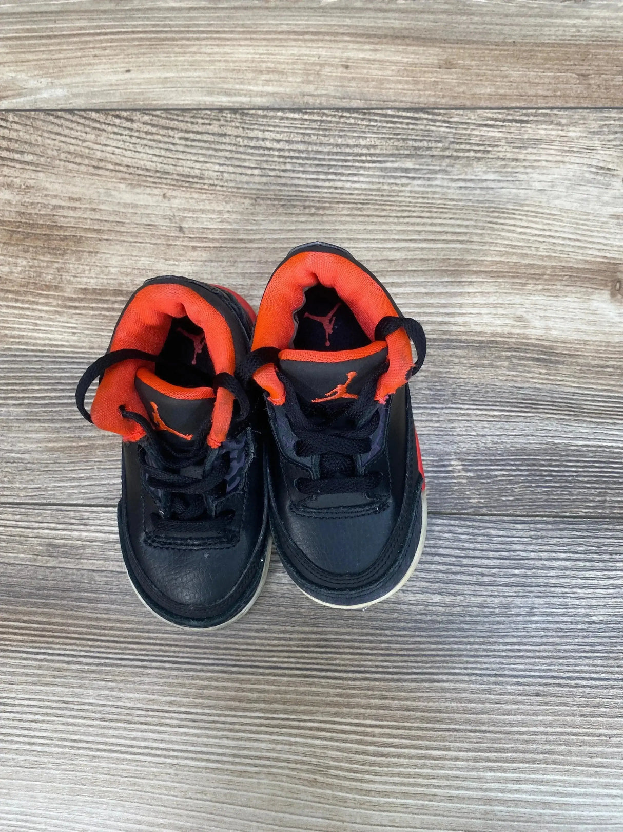 Top-down view of toddler black Air Jordan 3 Retro sneakers showing crimson padded collars and Jumpman logos on wood floor