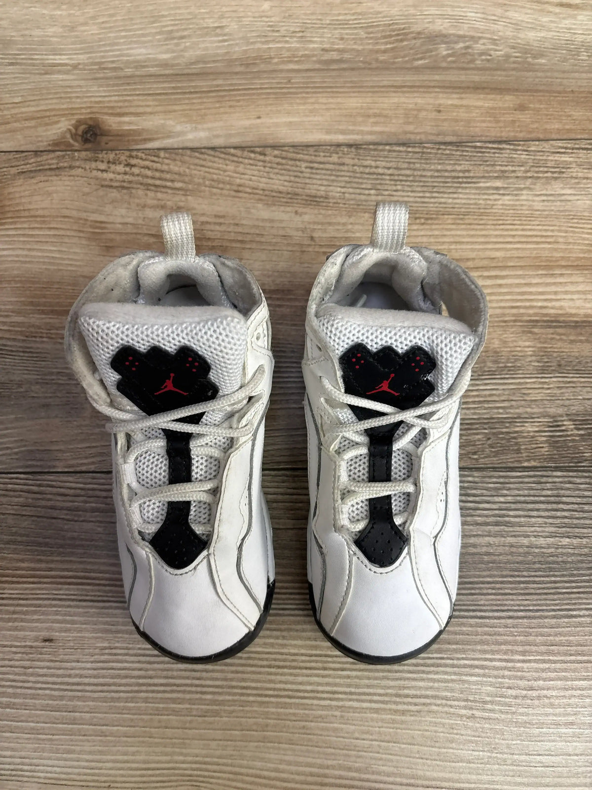 Pair of white toddler Air Jordan sneakers with black and red accents on wooden floor