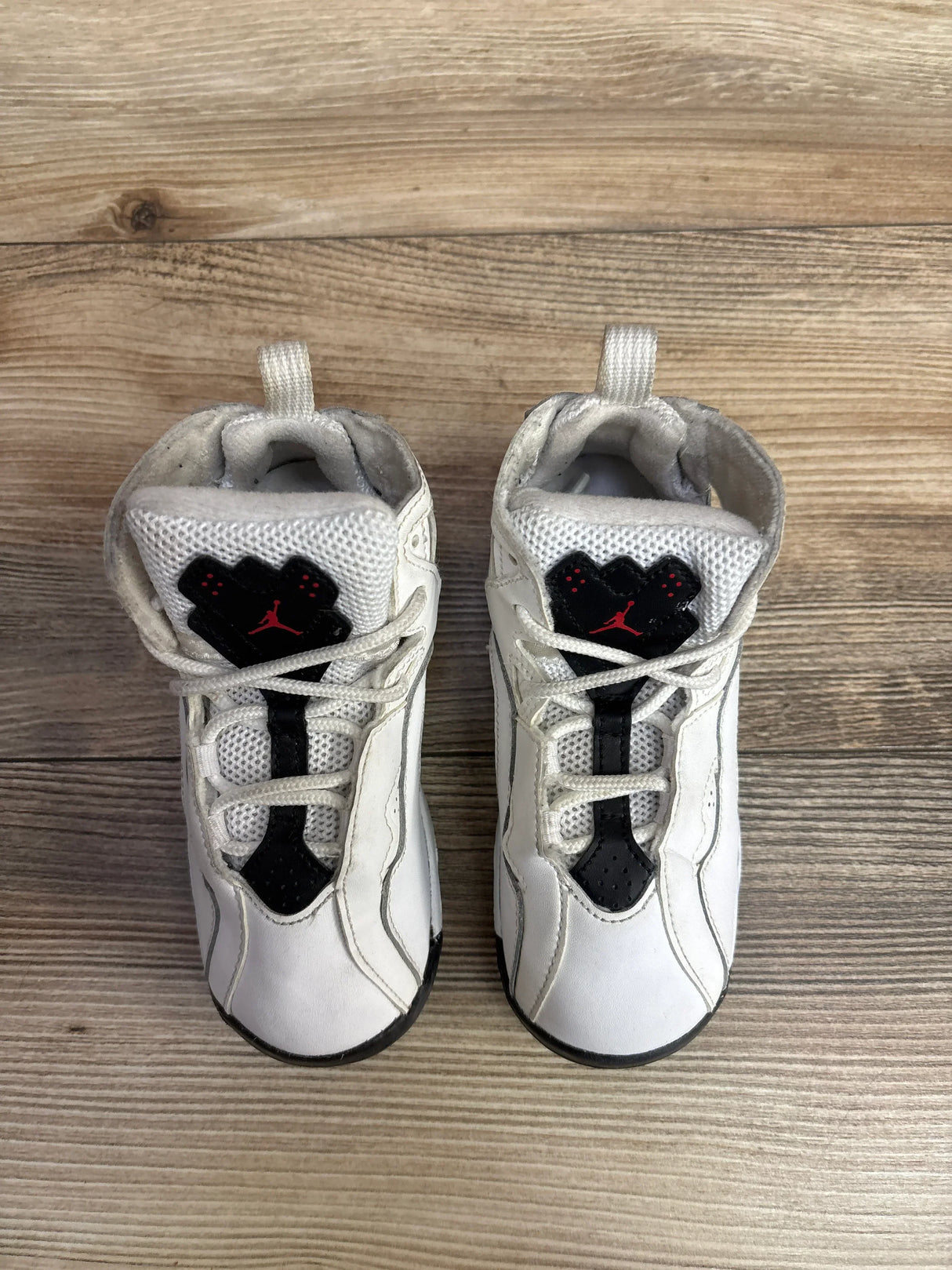 Pair of white toddler Air Jordan sneakers with black and red accents on wooden floor