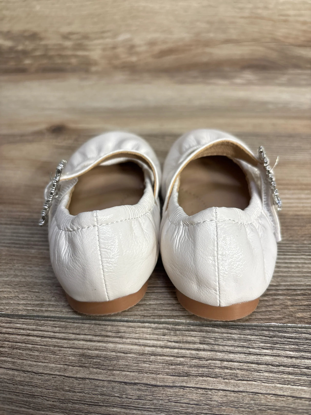 Back view of white leather ballet flats with tan soles on wooden floor