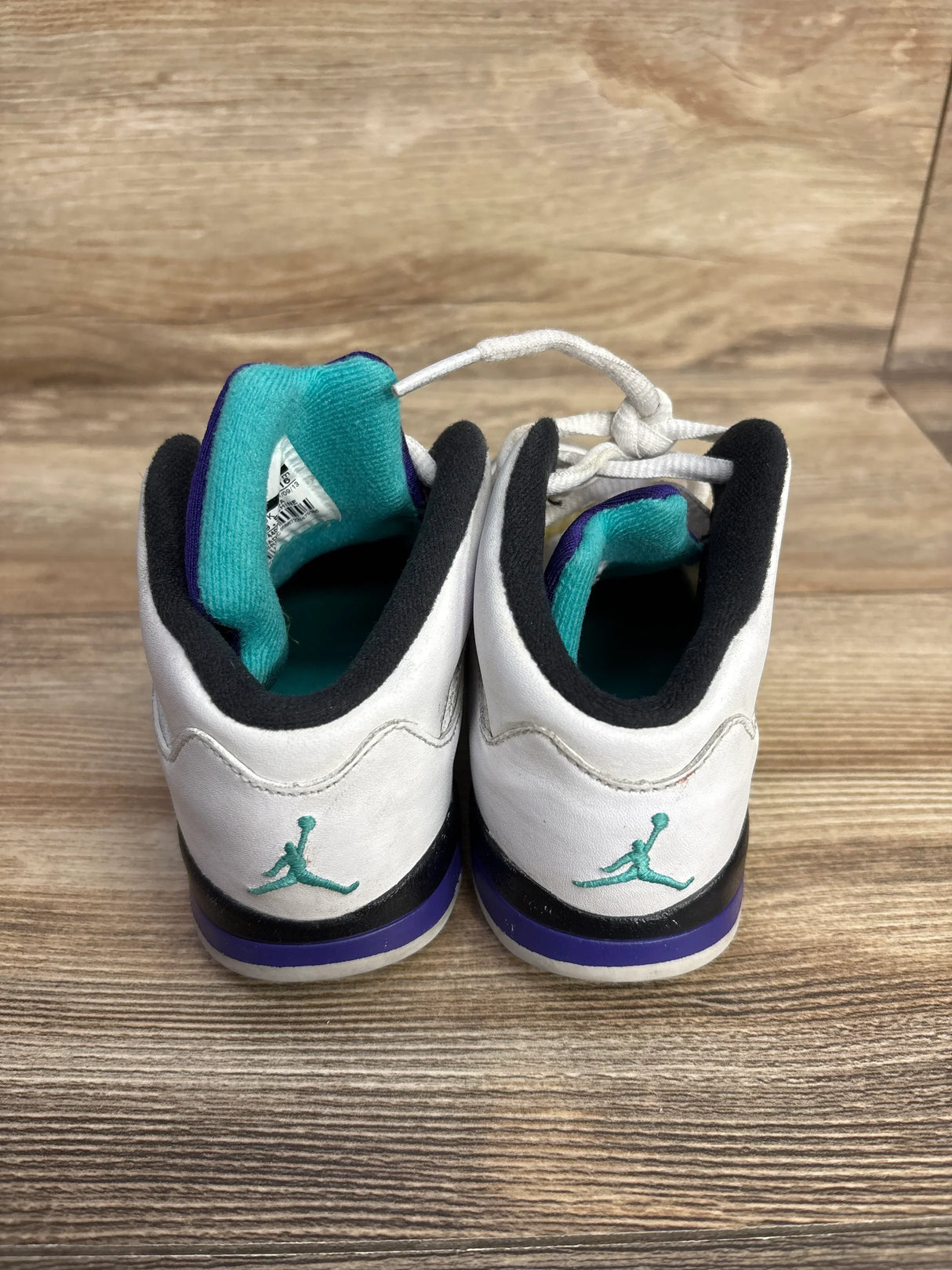 Pair of white, black, and purple toddler Air Jordan sneakers with turquoise inner lining on wooden surface