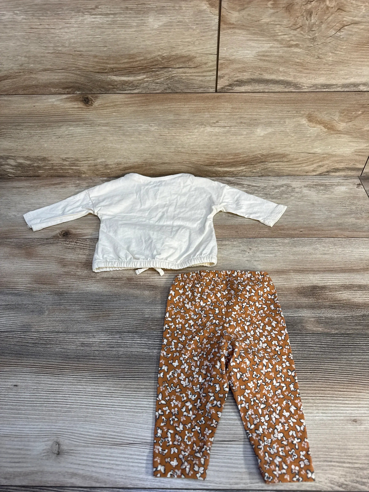Baby outfit with white long sleeve shirt and brown floral leggings on wood floor