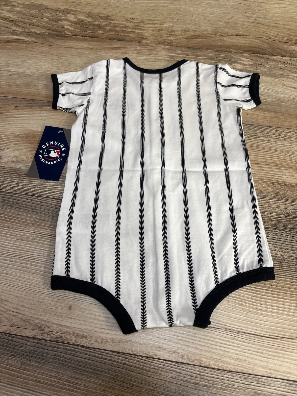 Flat lay front of white baby romper with black baseball-style pinstripes and black trim, MLB hang tag on wood background