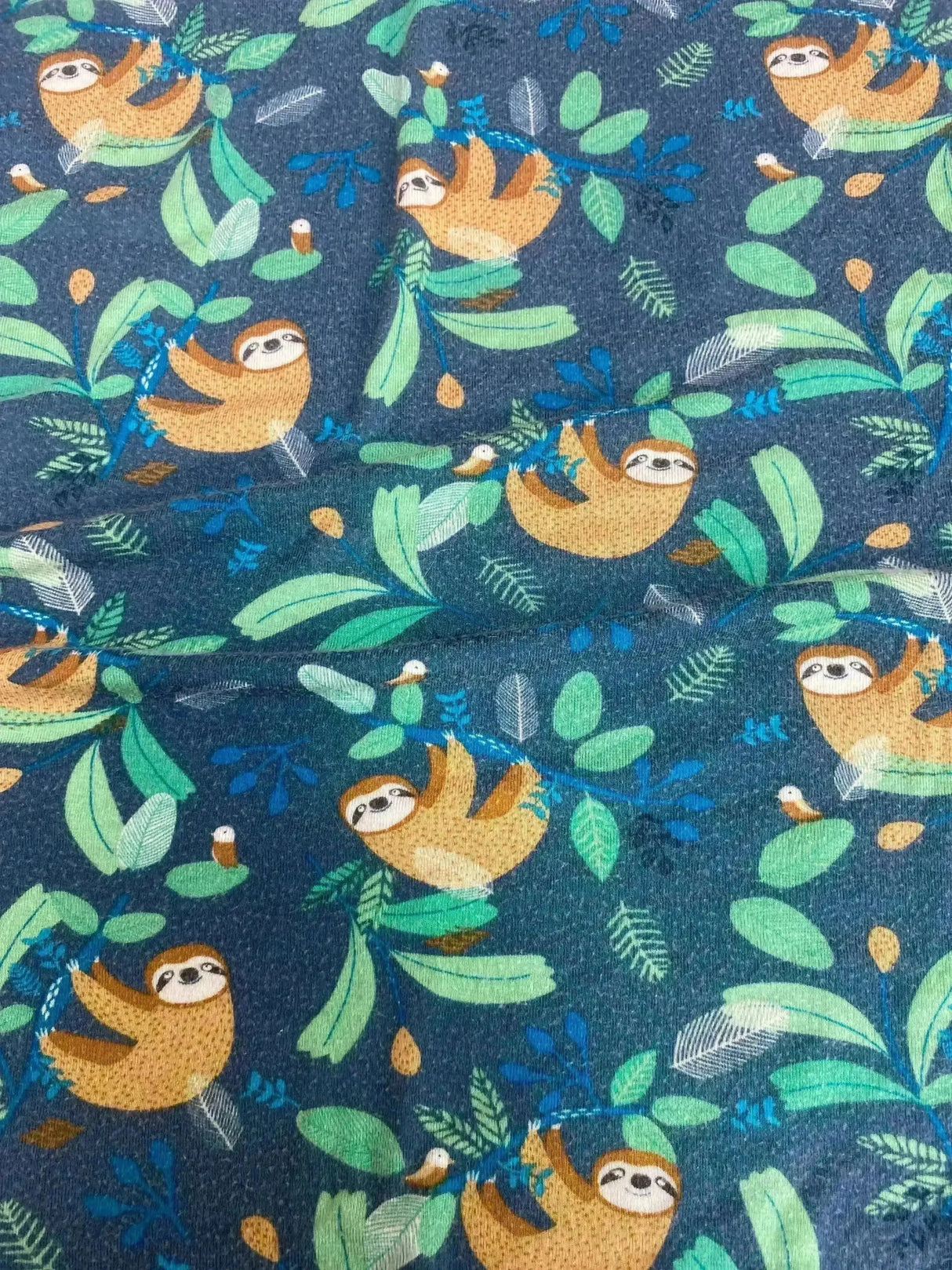 Close up of Milk Snob car seat and nursing cover, green sloth print, showing repeating sloth and leaf pattern on navy background