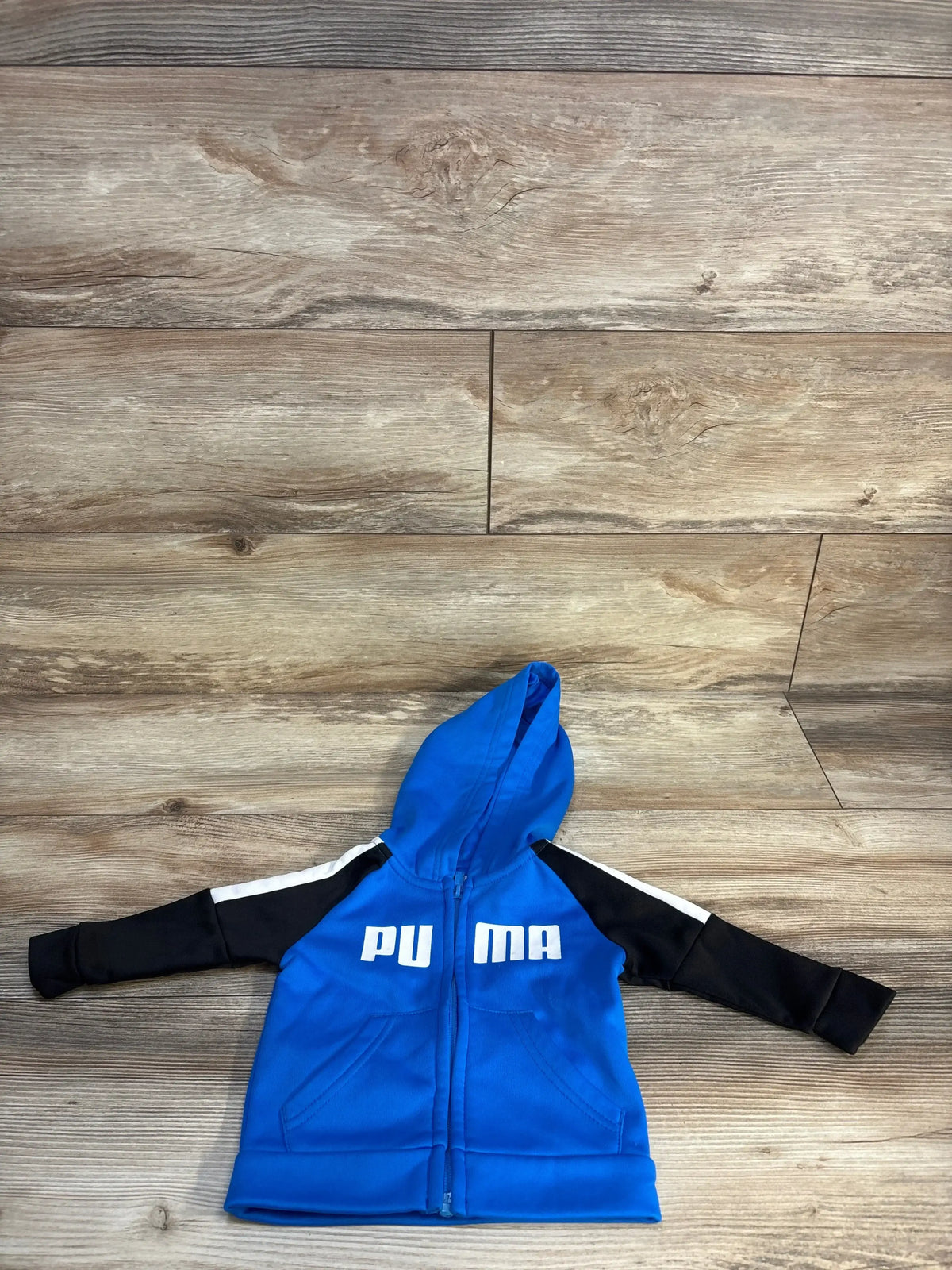 Blue and black kids' zip-up hoodie with white PUMA logo, laid flat on wood floor