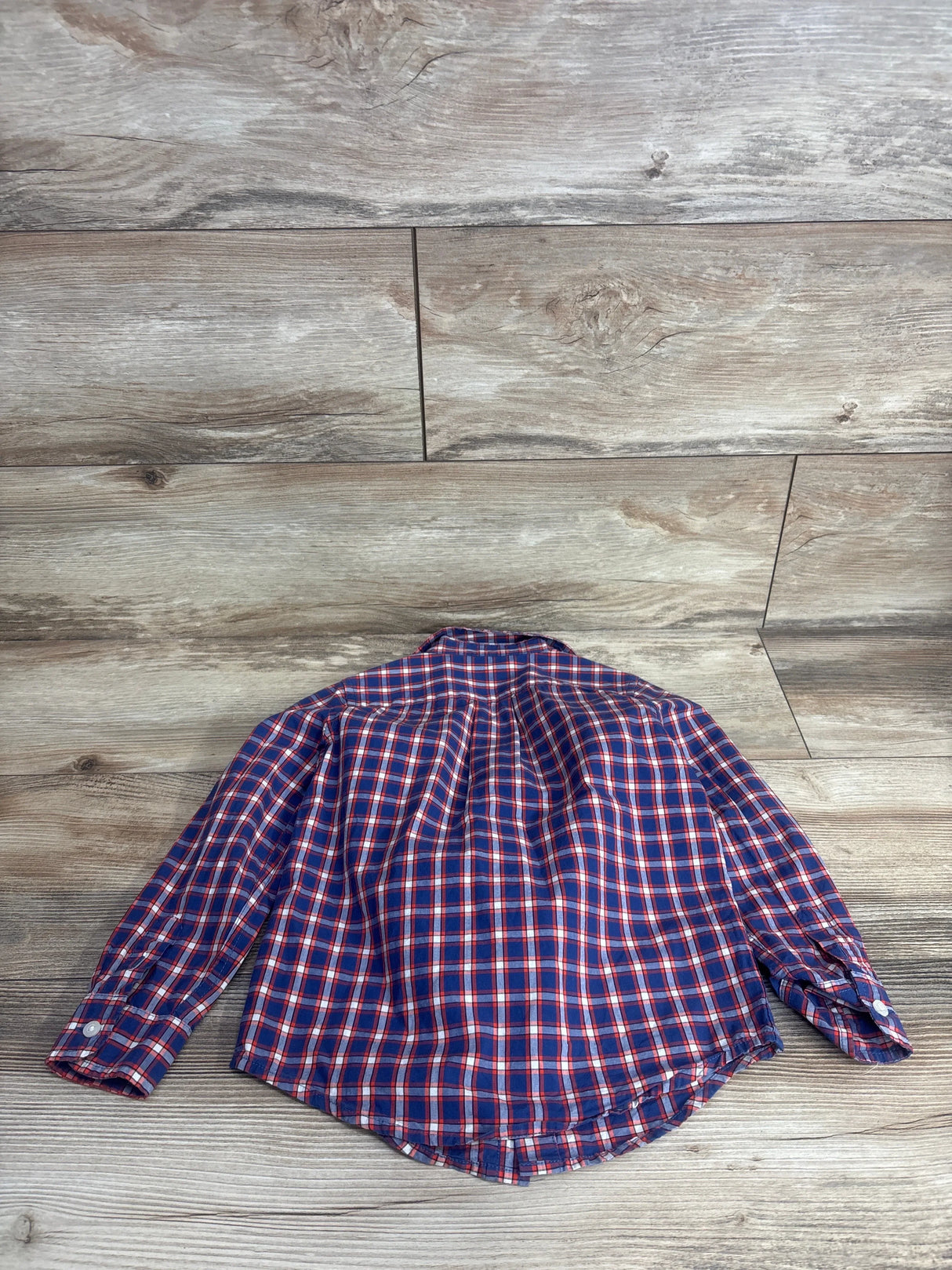 Navy and red plaid long sleeve kids shirt laid flat on wood background