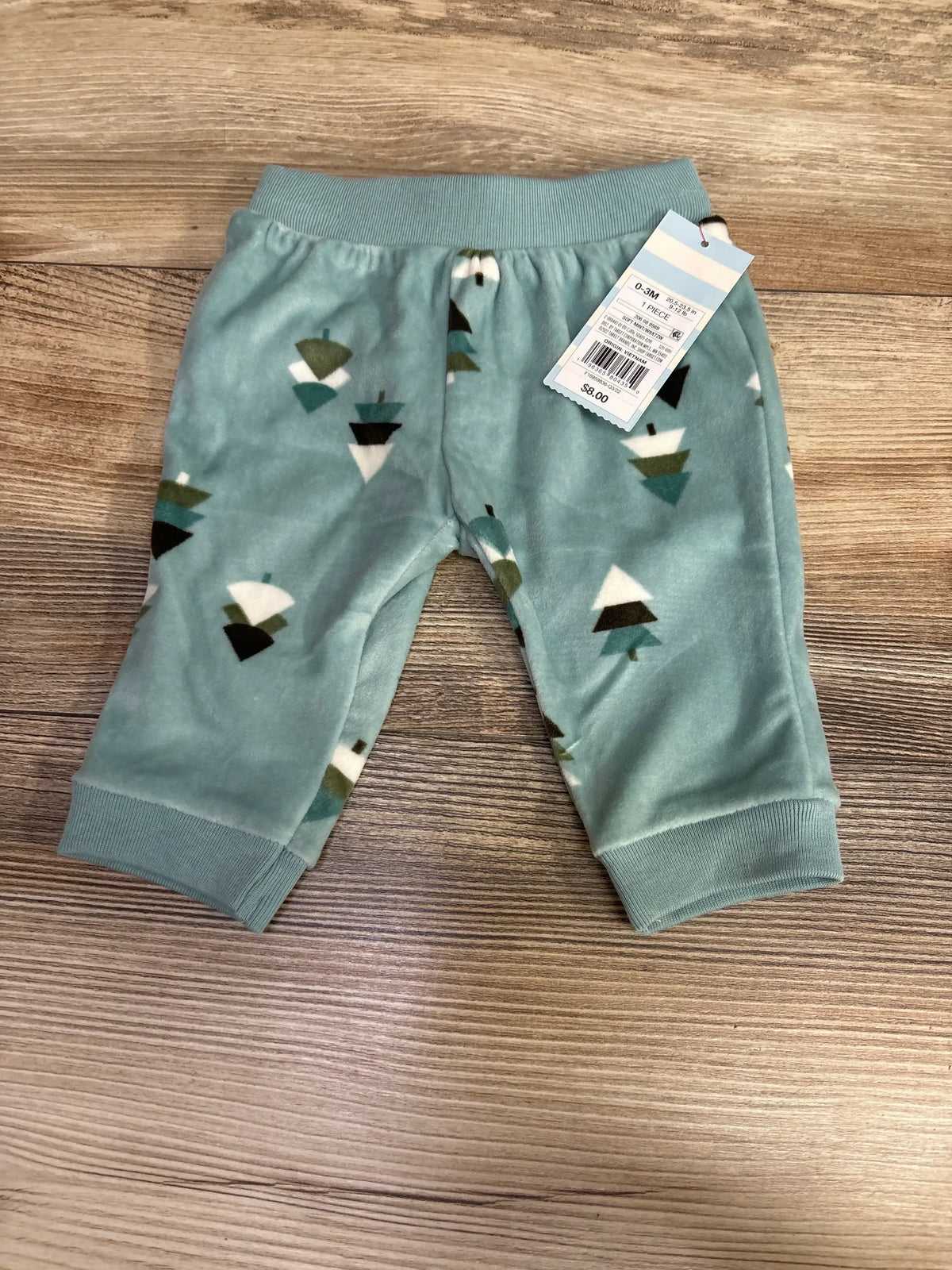 Top-down view of teal velour pull-on baby pants (0-3 months) showing tree print, ribbed cuffs, and elastic waistband on wood surface