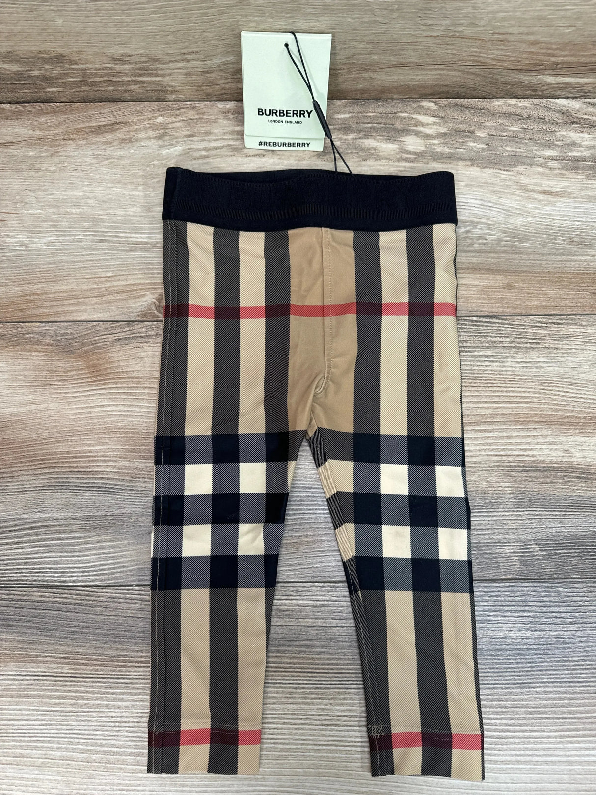 Front of Burberry baby leggings size 18M showing beige Gina check pattern and black elastic waistband on wood background