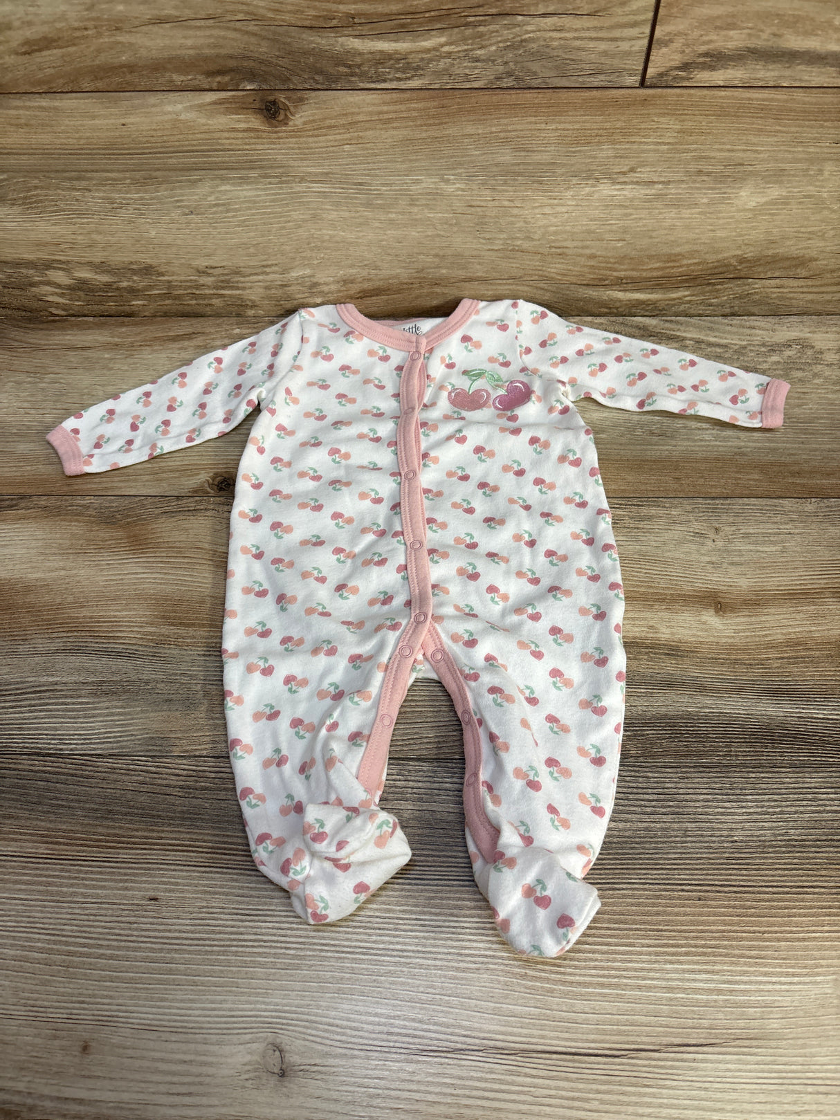 White baby onesie with pink cherry print and pink trim laid flat on wooden floor
