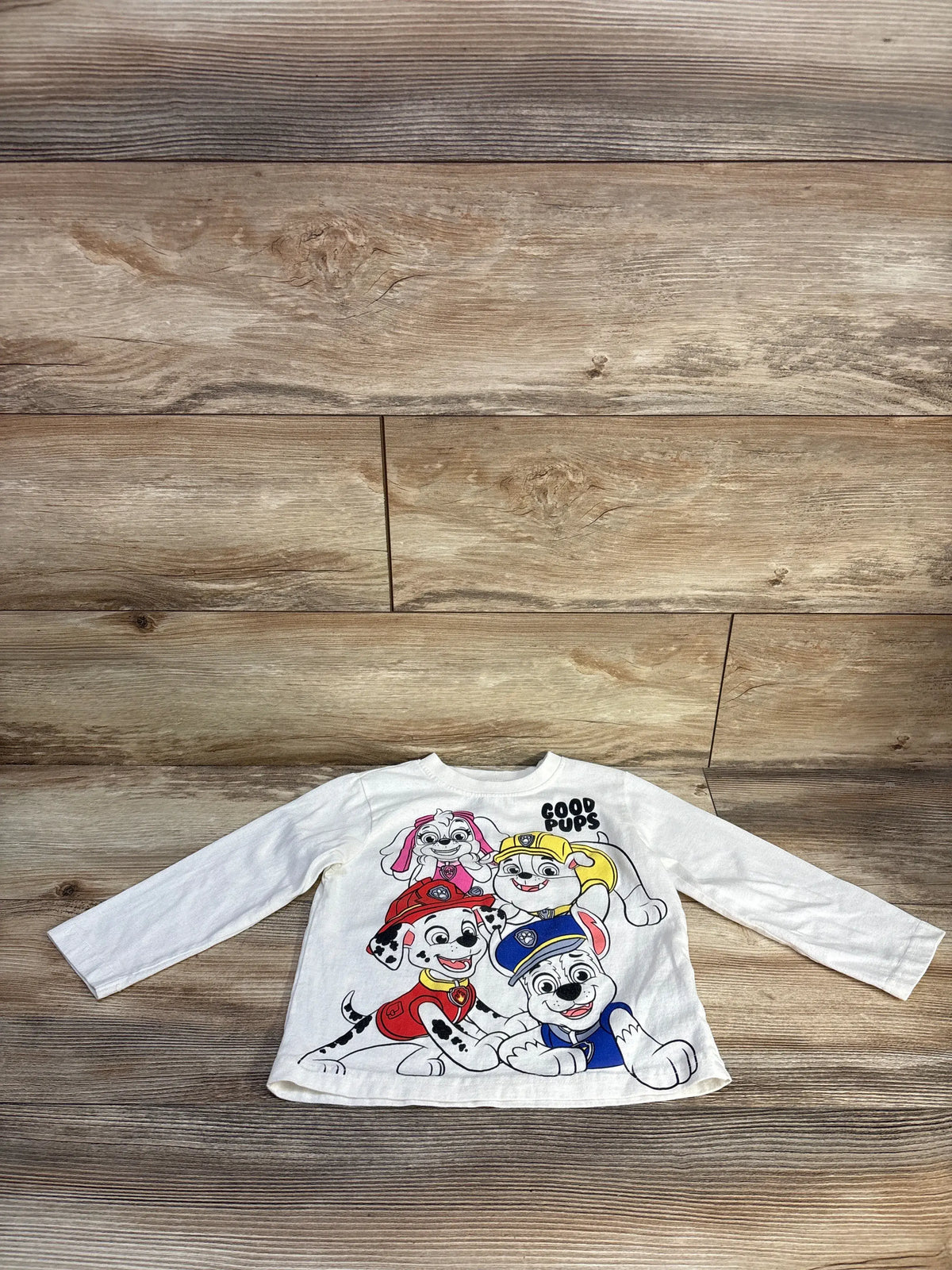 Front view of white Nickelodeon PAW Patrol shirt with colorful character graphics, GOOD PUPS text, and long sleeves on wood
