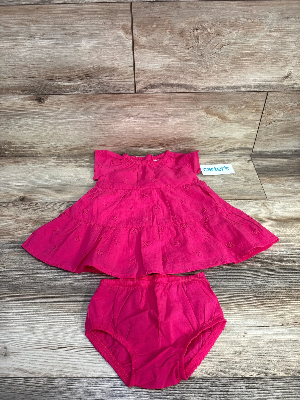 Front view of Carter’s hot pink eyelet tiered dress and matching bloomers showcasing tiered ruffles and eyelet embroidery on wood plank background