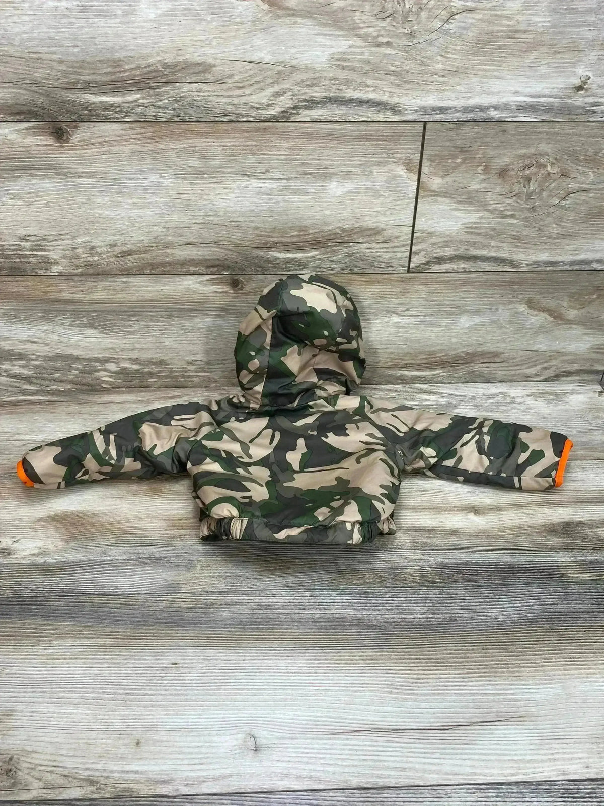 Back view of The North Face Perrito jacket, reversible green camo, hooded with elastic hem and orange cuffs on wood floor