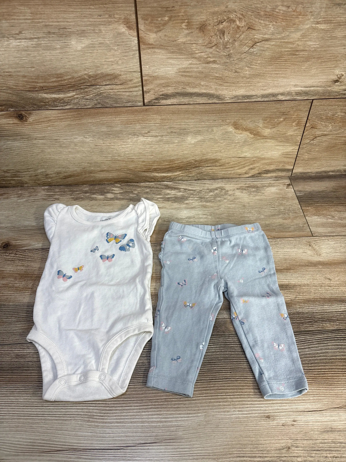 Front view of Carters two-piece baby outfit set showcasing a white butterfly bodysuit and butterfly-print pants on a wood floor