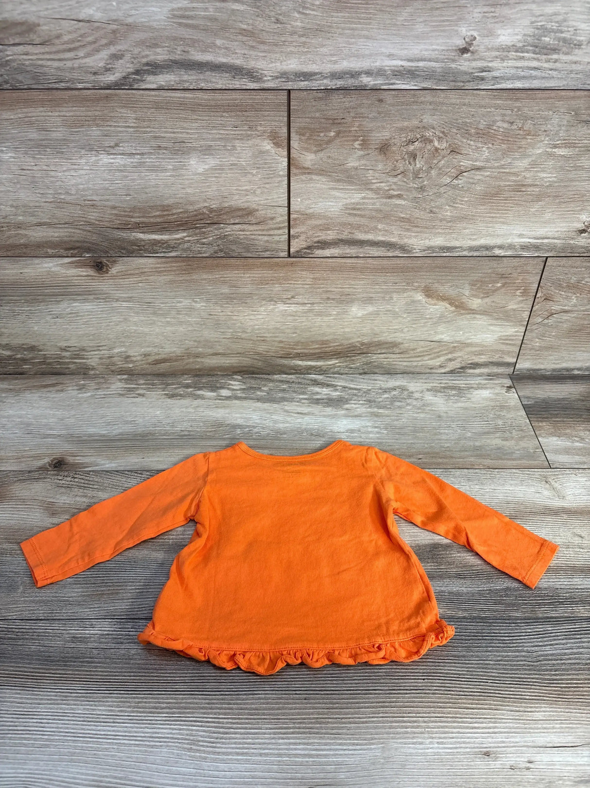Back view of Carter’s orange long-sleeve Happy Howl O Ween shirt in size 12 months showcasing a ruffled hem on a wood-look floor