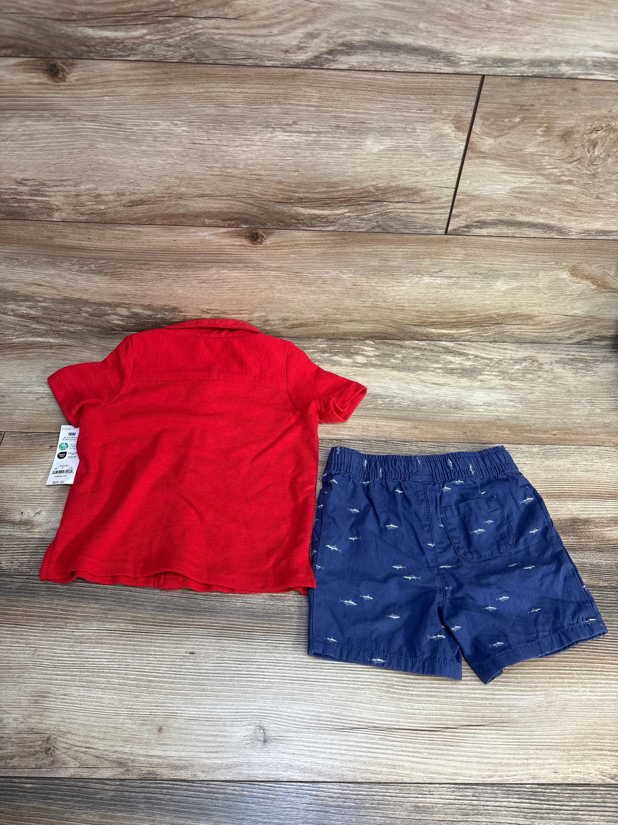 Red short sleeve toddler shirt and navy shark print shorts set on wood floor