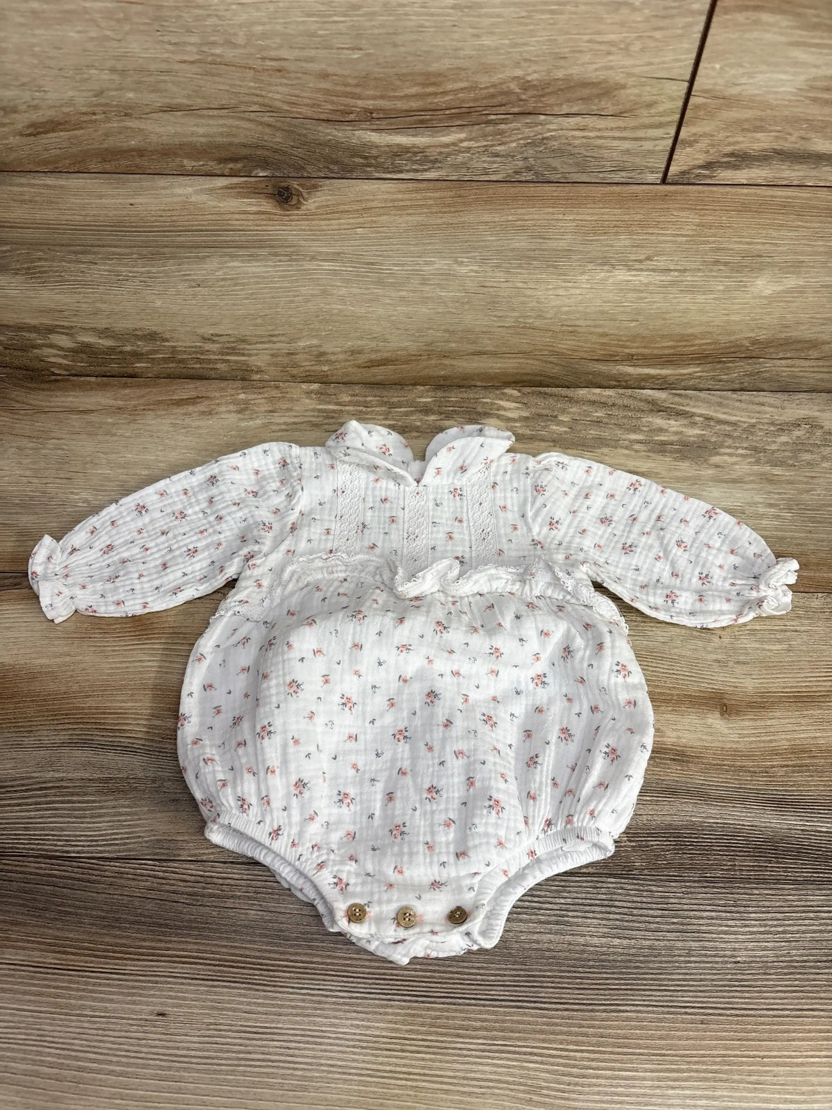White long-sleeve baby romper with small floral print and button snaps, laid on wood floor
