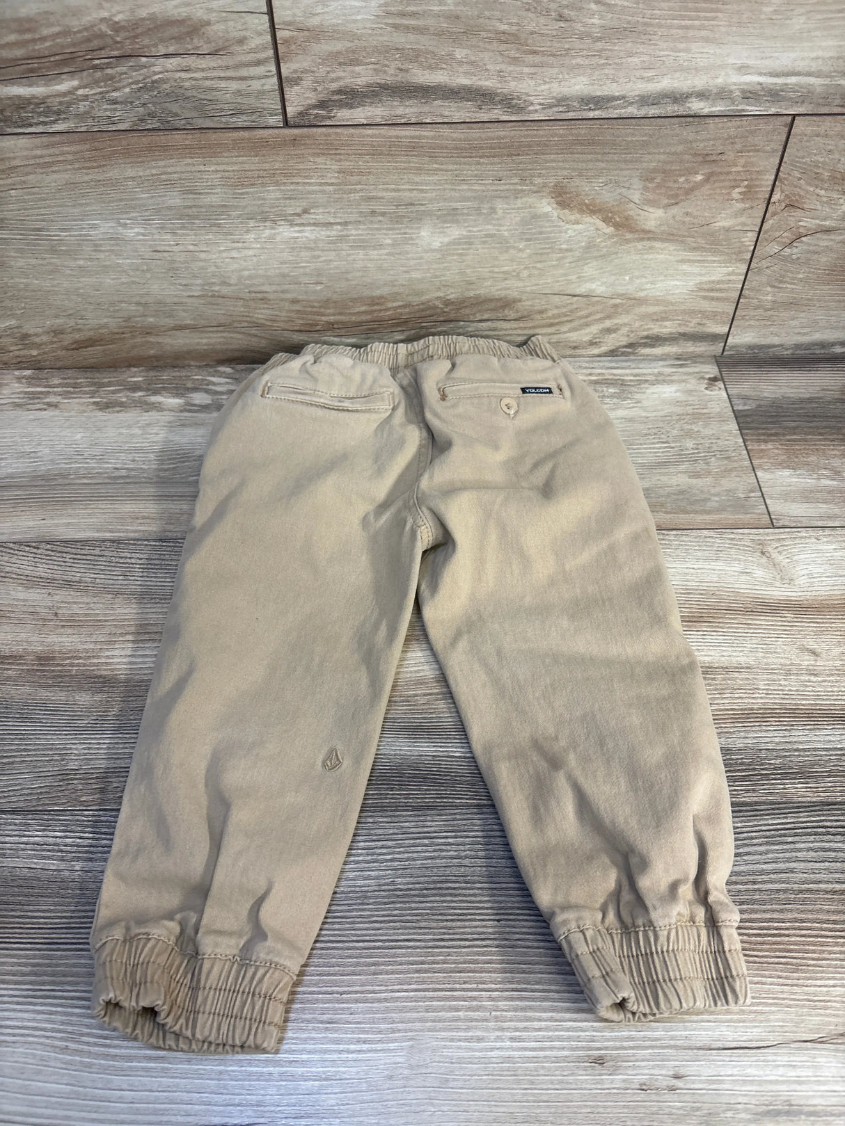 Beige Volcom kids jogger pants with elastic waist and cuffs, laid flat on wood floor