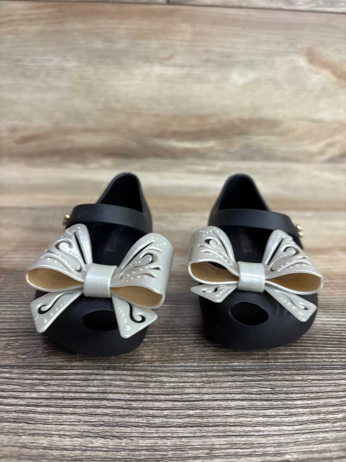Front view of Mini Melissa Ultragirl Bow black jelly flats size 5C showcasing cream decorative bows with wooden background