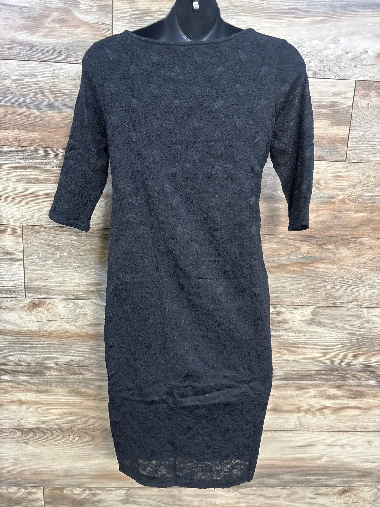 Front view of black lace fitted maternity dress with three-quarter sleeves on a black mannequin against a wood plank backdrop