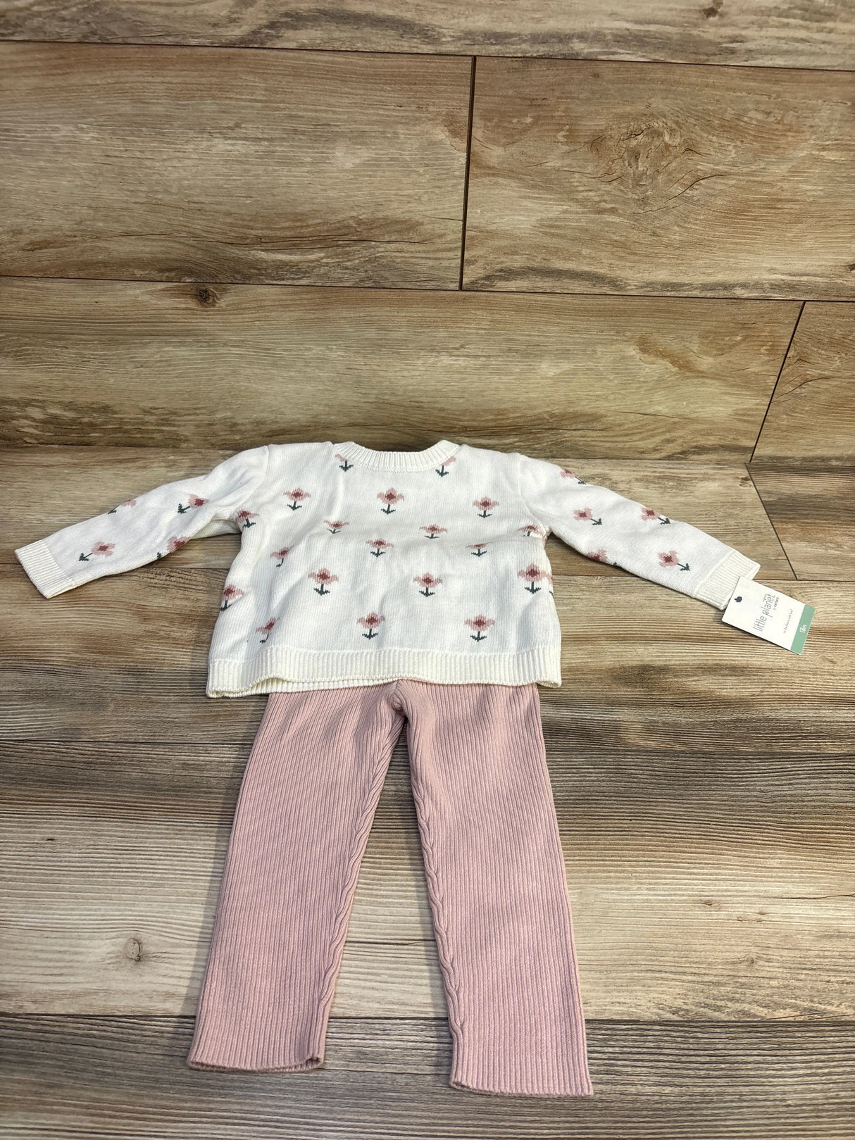 Flat lay of Little Planet Organic 2-piece floral sweater set showing cream sweater with small pink flowers and ribbed pink leggings on wooden floor