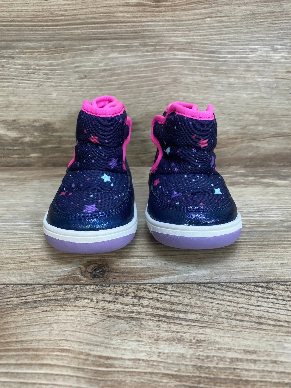 Front view of Surprize by Stride Rite Aster winter boots in navy showcasing star print pink fleece collar and lilac sole on wood plank floor