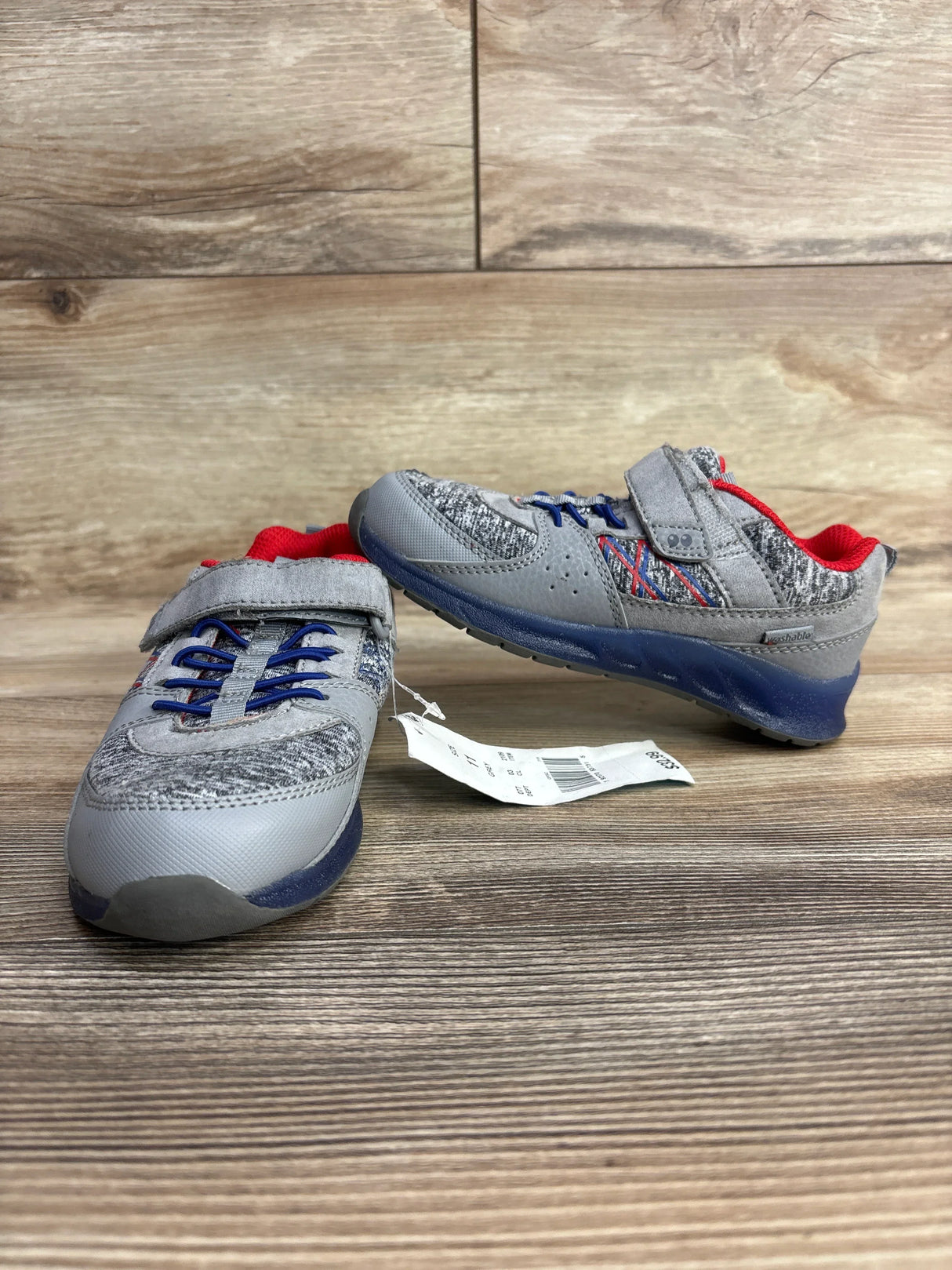Pair of gray and blue children's sneakers with red lining and Velcro straps on wooden surface