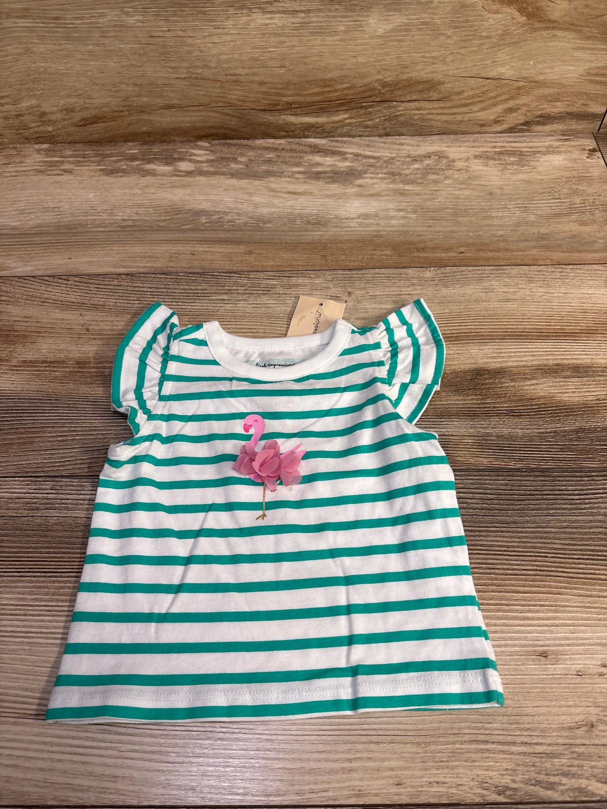 Flat lay of baby white and teal striped shirt showcasing a pink 3D flamingo applique and flutter sleeves on a wood background