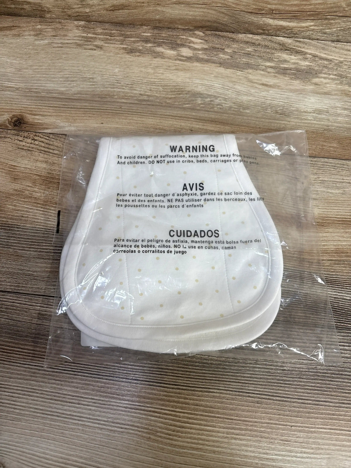 Top view of Oopsie Daisy burp cloths showing pale polka dots in clear plastic packaging with visible WARNING on wood