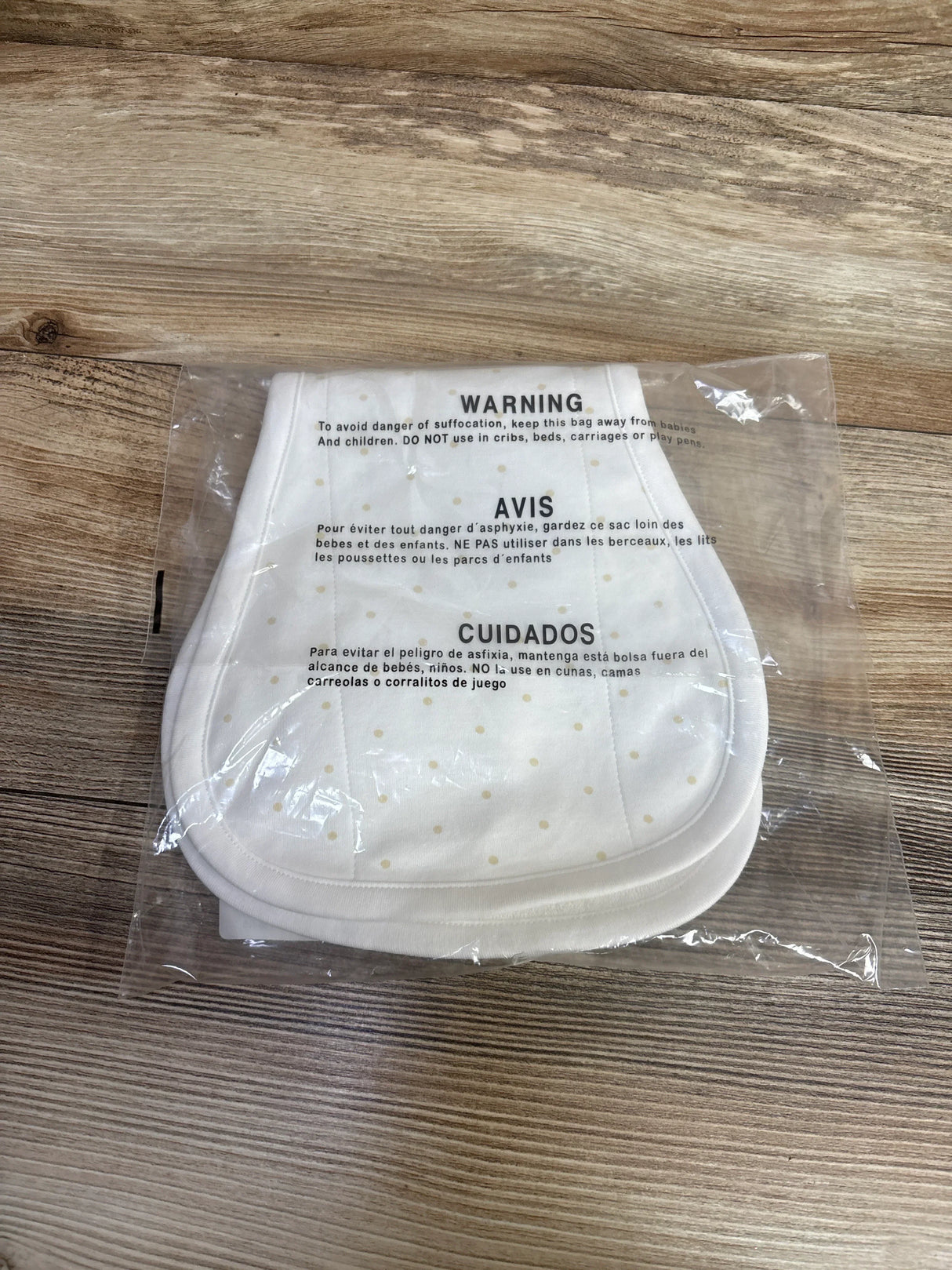 Top view of Oopsie Daisy burp cloths showing pale polka dots in clear plastic packaging with visible WARNING on wood