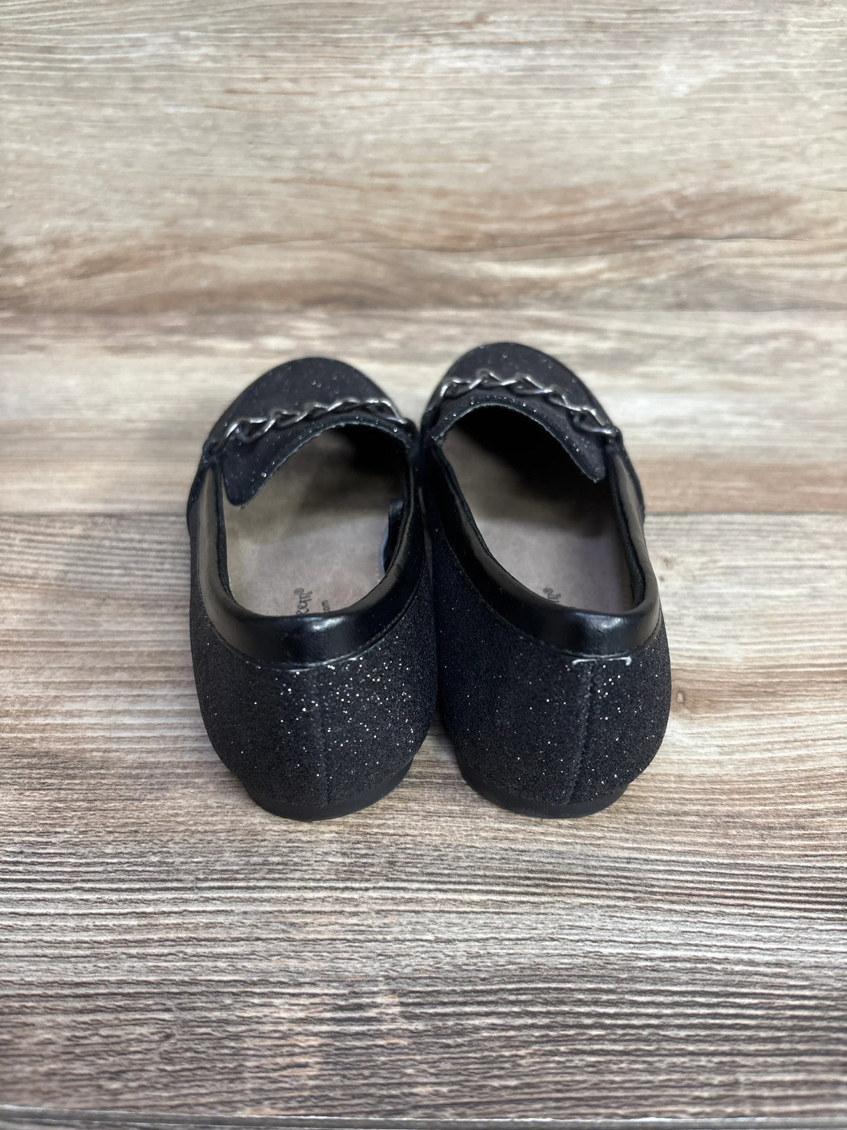 pair of black glittery ballet flats with chain detail on wooden surface