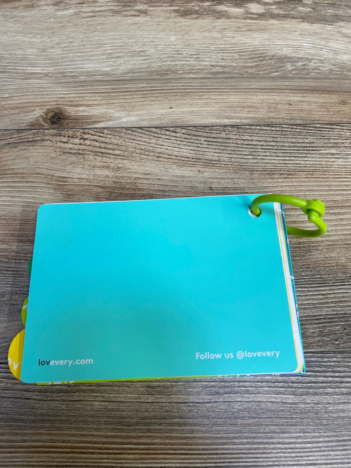 Blue Lovevery board book with green ring and website text on wooden surface
