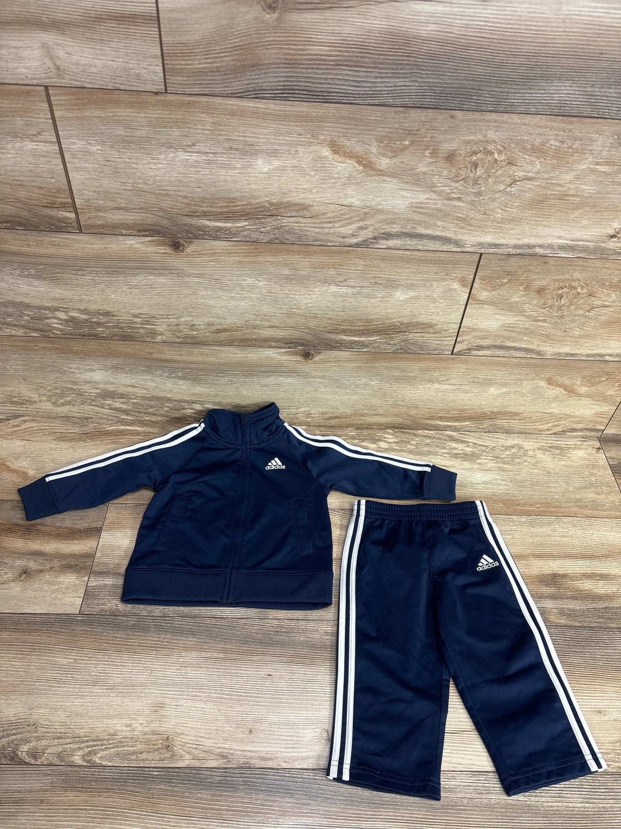 Children's navy blue Adidas tracksuit with white stripes, long-sleeve jacket and pants on wooden floor