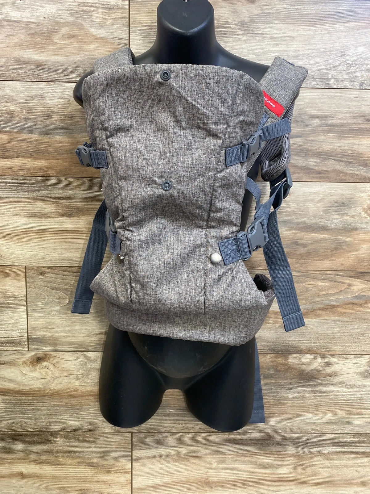 Front view of grey YOU+ME 4-in-1 carrier showcasing padded straps and adjustable buckles on black torso with wood background