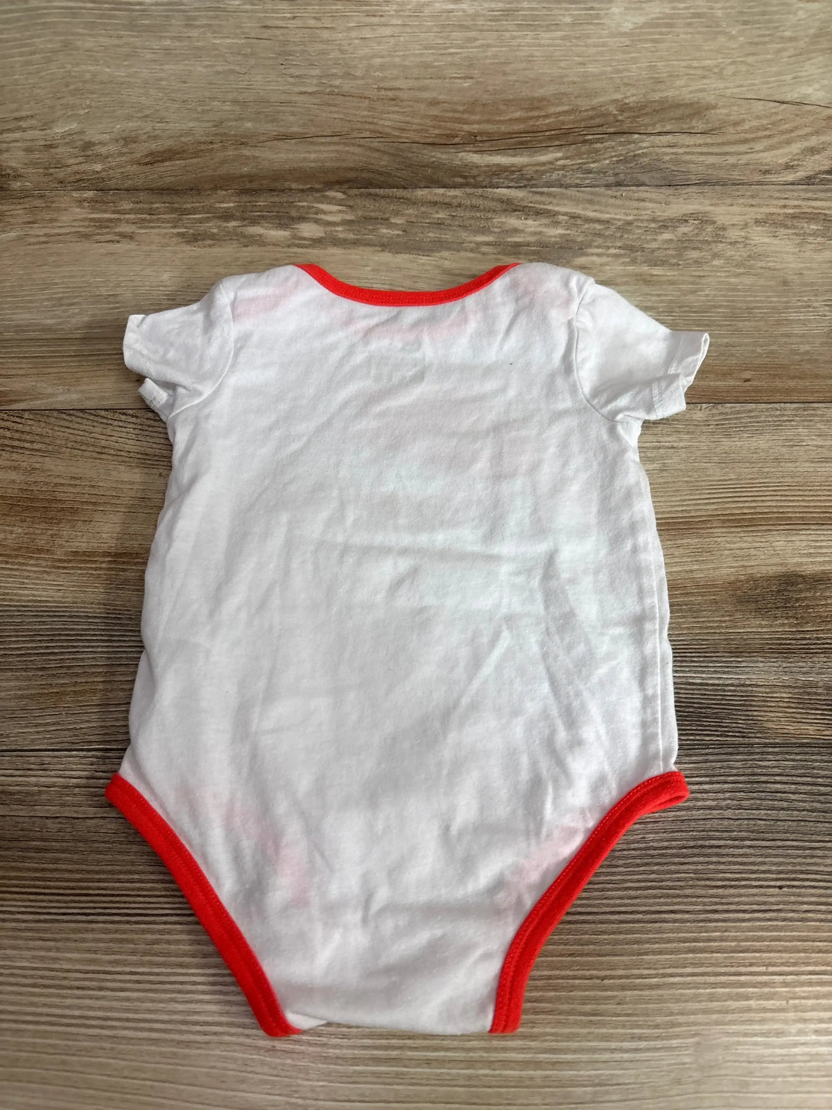 Front view of Nike Airmax Bodysuit White sz 6-12m showcasing red trim and short sleeves with a wood-grain background