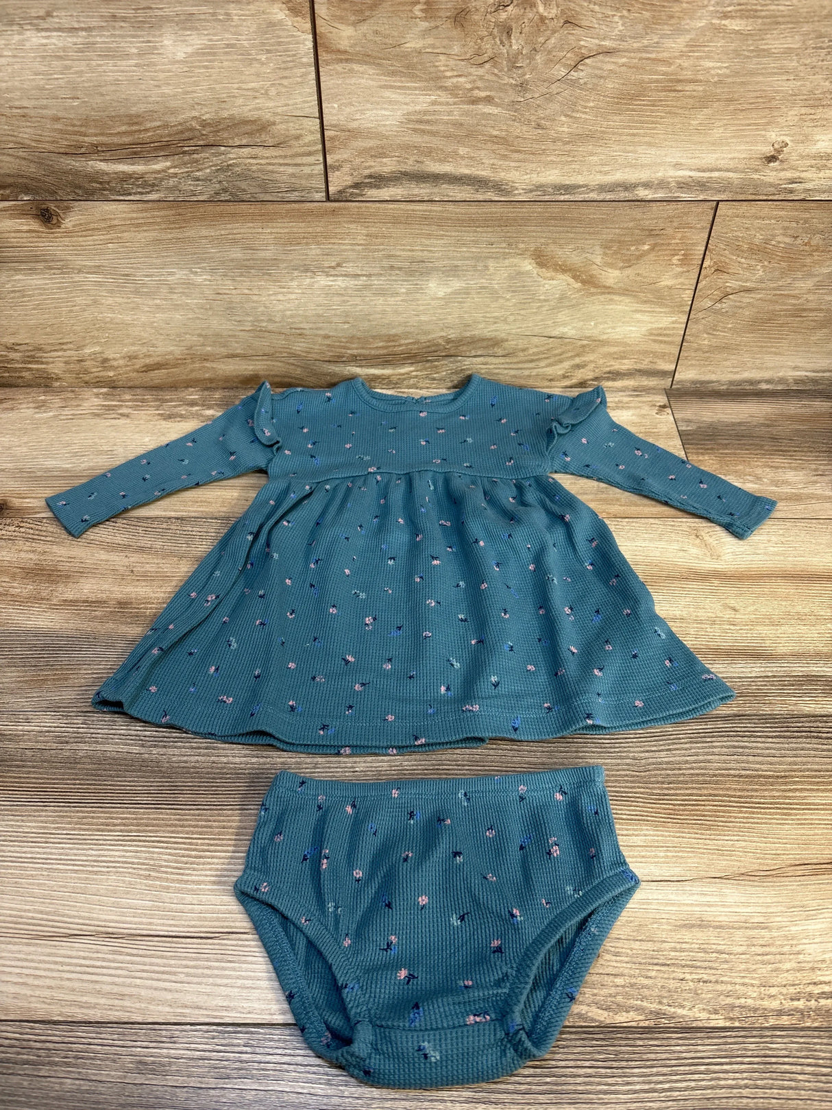 Flat lay of Carter’s teal waffle-knit long-sleeve baby dress with matching bloomers showing floral print on wood background