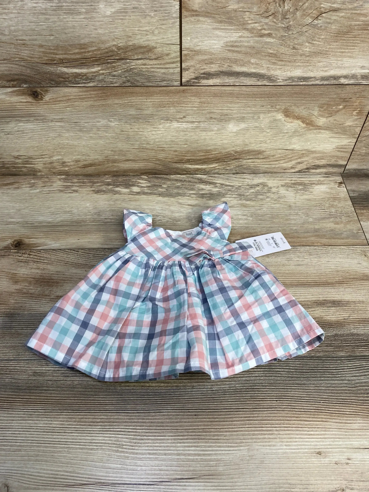 Flat lay of newborn 2pc plaid dress and bloomers in pastel checks, flutter sleeves and gathered skirt on wood