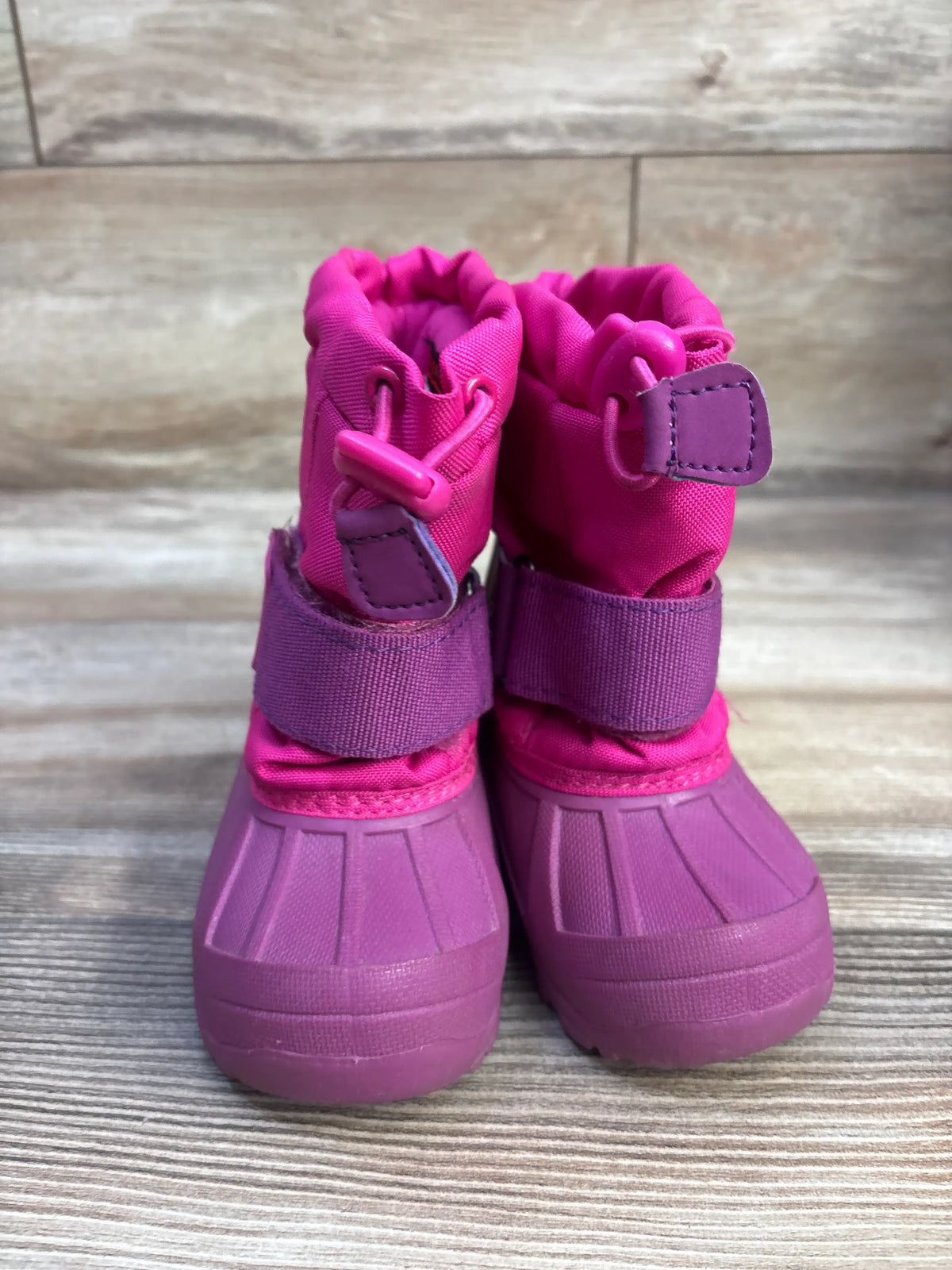 Front view of pink Thermolite snow boots in size 5/6C showcasing adjustable ankle straps and wide rubber soles on a wood-look surface