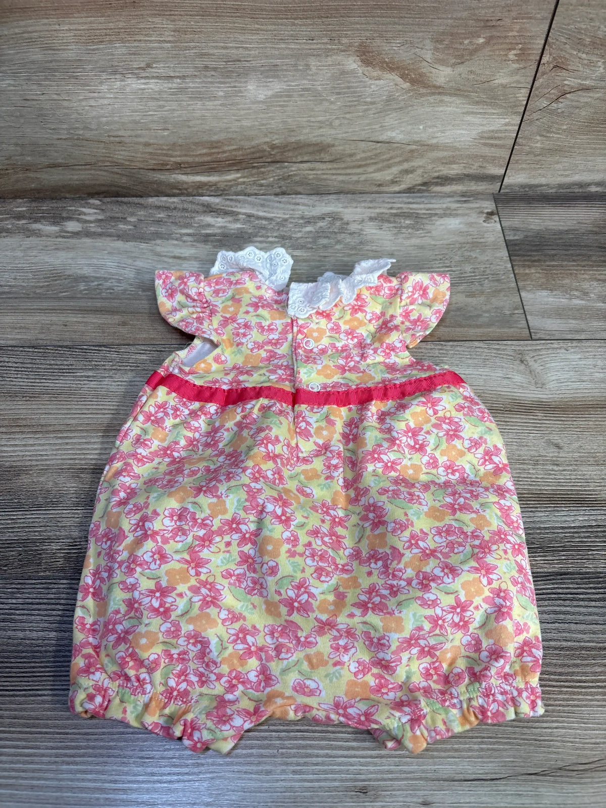 Front view of Laura Ashley yellow floral shortie romper showcasing white lace collar and red waist trim on a wood floor